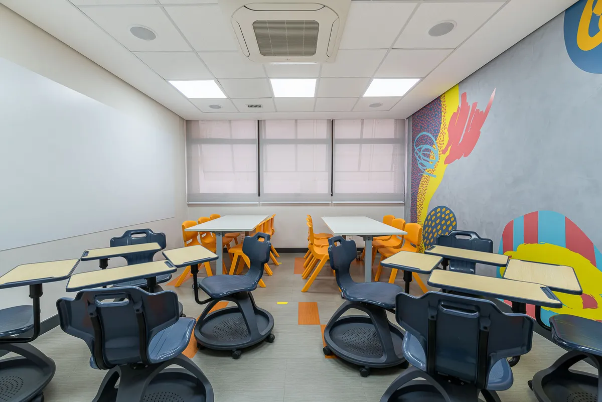 Sala de aula com cadeiras de rodízio e mesas modulares organizadas em grupos e mural colorido.